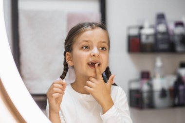 Banyoda aynaya bakarken dişleri dökülen beyaz bir kızın portresi. Heyecanlı ifade ve çocukluk dönüm noktası örgülü saçlar ve günlük kıyafetlerle taşınıyor..