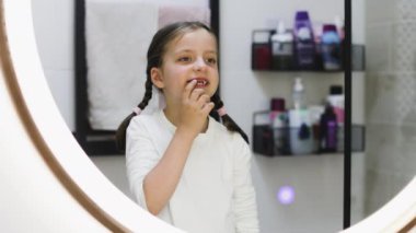 Banyodaki aynada ağzı işaret eden bebek dişleri düşmüş, gülümseyen beyaz kız portresi..