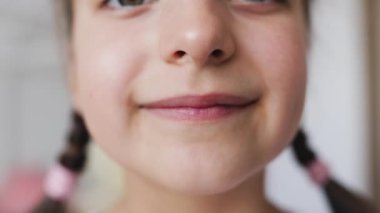 Dişleri eksik, gülümseyen beyaz bir kızın portresi. Evde bebek dişleri dökülürken oluşan boşluğu gösteriyor. Saçları örgülü kahverengi, çocukluğu ve diş kaybını temsil ediyor..