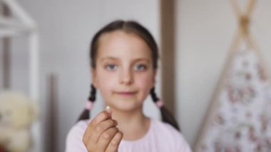 Küçük beyaz kız, bebek dişini içeride tutmaktan gurur duyuyor. Rahat ev ortamında ilk dişini düşürme heyecanı ve merakı yaşayan küçük bir çocuk..