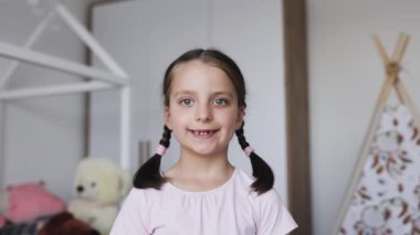 Süt dişlerini kaybettiği için saçlarını örmüş beyaz kız portresi. Korkunç bir ifadeyle evde poz veriyor..