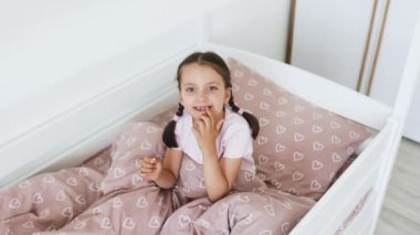 Saçları örgülü küçük beyaz kız heyecanla yastığın altına bebek dişi koyar. Diş perisinin beklentisi neşe getirir. Pembe kalp desenli yatak örtüsü yatma ayinine tuhaf bir dokunuş katar..