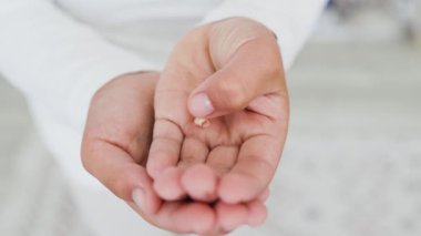 Bebek dişi tutan küçük çocuk elleri. Beyaz elbiseli beyaz çocuk, ilk dişini kaybettiği için heyecanlanıyor. Resim çocukluk dönüm noktalarını ve büyümeyi somutlaştırır.
