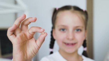 Yavru dişini gösteren küçük beyaz kız ev ortamında heyecan ve gurur hissederek düştü. Sembolik çocukluk dönüm noktası ve büyüyen an, parlak bir atmosferde yakalandı..