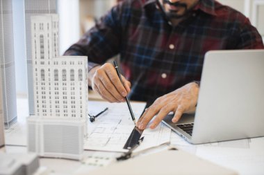 Hintli erkek mimar titizlikle modern şehir planını kalem ve cetvel kullanarak planlıyor. Çalışma masasında odaklanmış tasarım süreci.