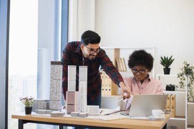 Hintli erkek ve Afrikalı kadın modern ofis ortamında mimari model üzerinde işbirliği yapıyorlar. Parlak doğal ışık ile yaratıcı takım çalışması atmosferi ve yenilikçi şehir tasarım kavramlarına odaklanma.