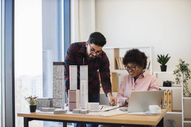 Hintli erkek ve Afrikalı kadın şehir modelleriyle birlikte mimarlık projesinde işbirliği yapıyorlar. Takım çalışması ve yaratıcılıkla ofis kurmak şehir planlamasını geliştiriyor. Profesyonel ortam gösterim tasarımı.