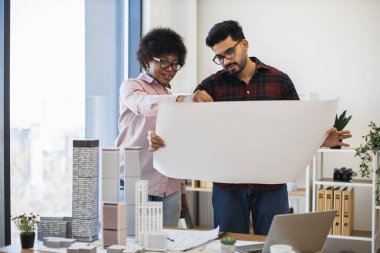 Hintli erkek ve Afrikalı kadın mimarlar modern şehir planlarını inceliyorlar. Mimari modeller, takım çalışması ve işbirliği ile ofis ayarları. Planlamaya ve tasarlamaya odaklan.