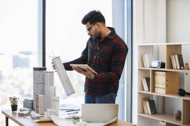 Genç Hintli erkek mimar şehir modelini oluşturmak için dijital araçlar kullanarak şehir projesinde çalışıyor. Modern tasarım ve teknoloji entegrasyonuna odaklanmış.