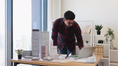 30 'lu yaşlardaki Hintli erkek mimar, dizüstü bilgisayar ve ölçekli modeller kullanarak modern şehir tasarım projesi üzerinde çalışıyor..