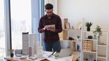 Modern ofisteki Hintli erkek mimar, şehir projesini model binalarla geliştirmek için dijital tablet kullanarak yaratıcılık ve konsantrasyonu vurguluyor..