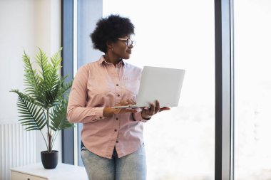 Güncel ofis ortamında dizüstü bilgisayar kullanan Afro-Amerikalı iş kadını. Profesyonel çalışma, teknoloji kullanımı ve üretkenlik kavramı.