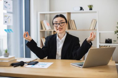 İş elbiseli Asyalı kadın, stres atmak için ofis molası sırasında Lotus pozisyonunda meditasyon yapıyor.