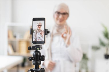 Başörtülü Müslüman kadın telefonda şifa dersi veriyor, sağlık tavsiyelerini paylaşıyor. Genç yetişkin tıp uzmanları sosyal medya platformunu kullanarak izleyicileri sağlık tavsiyelerine dahil ediyorlar..