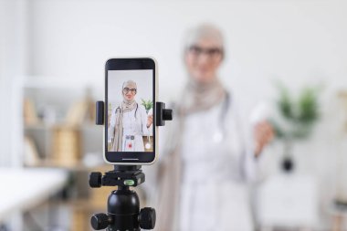 Modern ortamlarda tıp üzerine video dersi kaydeden Müslüman bir kadın. Orta Doğulu yetişkin, geleneksel ve dijital sağlık bilinçlendirme yöntemlerini birleştirerek, tedavi ipuçlarını çevrimiçi olarak paylaşıyor.