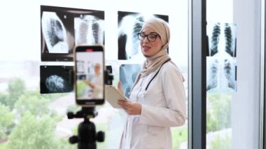 Genç Müslüman kadın doktor röntgenleri kullanarak online eğitim kayıtlarını tutuyor. Kamerada tıbbi kavramları anlatırken gözlük takıyor ve tesettür yapıyor..