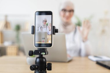 Kendine güvenen genç Müslüman kadın doktor akıllı telefondan video dersi alıyor. İnternet platformu üzerinden tıbbi bilgilerini paylaşan bir kadın sağlık uzmanı. Eğitim kavramı, iletişim.
