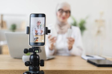 Orta Doğulu Müslüman kadın tıp üzerine video dersi kaydediyor. Seyirciyi üç ayaklı, dizüstü bilgisayarlı ve tabletli akıllı telefondan bağlar.