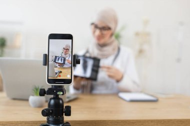 Orta Doğulu Müslüman kadın blogcu, akciğer röntgeni kullanarak bilgilendirici video dersleri kaydediyor. Genç bayan eğitimci, akıllı telefon kamerasıyla tıbbi görüşlerini paylaşıyor. Çevrimiçi eğitim ve sağlık hizmetleri kavramı.