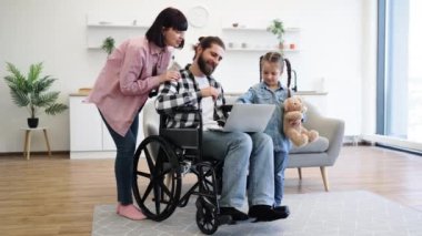 Modern mutfakta beyaz bir aile, anne tekerlekli sandalyede sakat bir baba, oyuncak ayıyla genç bir kız. Sıcak aile anları sevgi ve destek gösteriyor..
