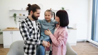Beyaz anne ve baba, parlak mutfak ortamında kızlarını kollarında tutuyorlar. Mutluluk ve aile bağlarını gösteriyorlar..