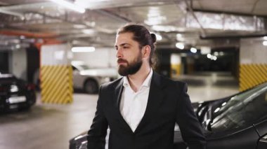 30 'lu yaşlarda, otoparkta duran kendine güvenen beyaz erkek işadamının portresi. Kollar çapraz, resmi takım elbise giyme, profesyonellik ve şehir ortamında başarı taşıma.