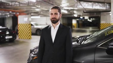 Takım elbiseli beyaz bir erkek yeraltı otoparkında düşünüyor. Kendinden emin ifade ve profesyonel görünüş kentsel iş liderliği ve başarı ortamı yaratıyor.