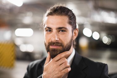 Takım elbiseli beyaz bir erkek yeraltı otoparkında düşünüyor. Kendinden emin ifade ve profesyonel görünüş kentsel iş liderliği ve başarı ortamı yaratıyor.