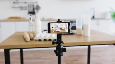 Modern mutfakta, yemek malzemeleri ve bulanık arkaplan içeren üç ayaklı telefon kayıt videosu. Yemek hazırlama süreci, özel dersler, yemek pişirme videoları veya blog yazma için ideal