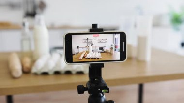 Akıllı telefon ile modern mutfak düzeneği un, yumurta, süt gibi yemek malzemelerini yakalıyor. Yemek tarifleri ya da video eğitimi için mükemmel bir şekilde düzenlenmiş çalışma alanı.