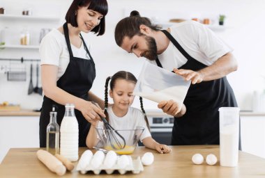 Kafkas ailesi mutfakta küçük bir çocukla yemek pişiriyor. Yemek tarifi için yumurta çırpıyor.