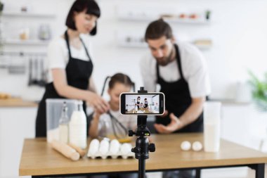 Beyaz ebeveynler ve çocuklar aile aktiviteleri sırasında çevrimiçi yemek videosu çekerken birlikte yemek pişiriyorlar.
