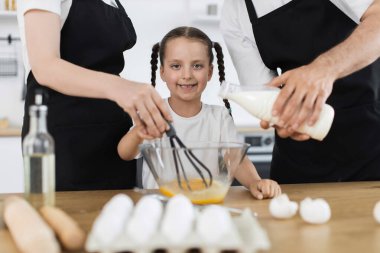 Mutfakta beyaz bir aile malzemeleri hazırlıyor. Genç bir kız çırpıcıyla karıştırıyor..