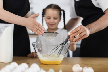 Mutfakta birlikte yemek pişiren beyaz bir aile. Ebeveynler ve çocuklar çırpıcı kullanarak vurucuyu hazırlayın.