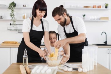 Kafkas ailesi parlak mutfakta yemek pişiriyor, iki yetişkin ve bir çocuk birlikte çalışıyor neşeli anlar yaratıyorlar, önlük giyip hamuru karıştırıyorlar, yemek malzemeleriyle çevrelenmişler.