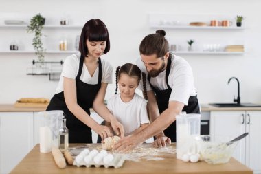 Kafkas ailesi yemek pişirme faaliyetleri için işbirliği yapıyor ve kaynaşıyorlar, aralarında baba, anne ve genç kız, mutfak tezgahında hamur yoğuruyorlar.