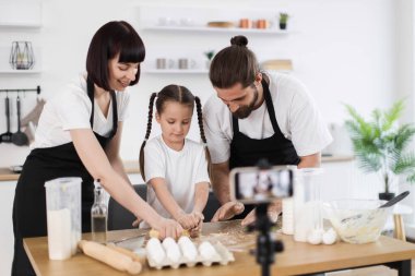 Aralarında genç kız ve iki yetişkinin de bulunduğu üç kişilik Kafkas ailesi, modern mutfak ortamında yemek vlog 'u oluştururken masaya hamur yoğurarak aile bağlantısını, yaratıcılığı vurguluyor.,