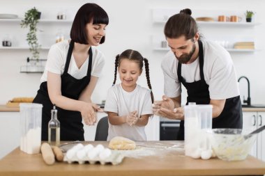 Gülümseyen genç anne-baba ve kız mutfakta para kazanıyorlar, mutlu bir bağ kuruyorlar.