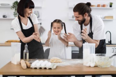 Parlak modern mutfak ortamında birlikte yemek pişiren ebeveynler ve çocuklardan oluşan aile, neşe ve işbirliği sergiliyor..