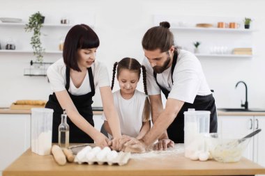 Beyaz bir aile mutfakta yemek pişiriyor ve birlikte eğleniyorlar. Anne, baba ve kız önlük giyip hamurla çalışıyorlar. Mutfak un ve malzemelerle dolu. Mutlu bir bağ kurma zamanı..