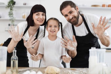 Küçük kızları mutfakta yemek pişiren, un kaplı yüzleri ve elleri olan beyaz anne babalar. Aile bağlarını, birlikteliği ve mutluluğu yemek yaparak yakalar..