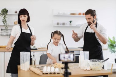 Beyaz aile mutfakta birlikte yemek pişiriyor, blog yazarları olarak içerik yaratıyor, dans ediyor ve gülümsüyor. Mutfak etkinliği, eğlence ve aşçılık becerilerinin karışımı ile güçlü bağları vurgulamak