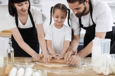 Mutfakta beyaz bir aile yemeği. Genç bir kadın, çocuklu bir adam yemek pişirmekten zevk alıyor. Mutluluk ve sevgi ifadeleri.