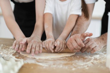 Hem yetişkinlerden hem de çocuklardan oluşan aile mutfakta hamur hazırlamakla meşgul. Birlikte çalışan insan elleri aile bağını ve yemek pişirme ve pişirme çabalarını sembolize eder..
