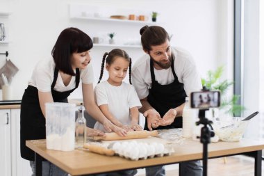 Kafkasyalı ebeveynler ve çocuklar mutfakta akıllı telefonla yemek pişiriyor ve video çekiyor.