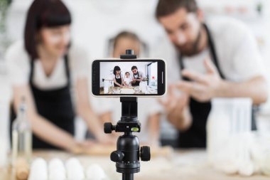 Beyaz bir aile, pişirme sürecini gösteren parlak ev mutfağında yemek pişirme dersleri videosu hazırlıyor..