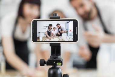 Kafkasyalı ebeveynler ve genç kız birlikte hamur yoğurarak blog yazarları olarak içerik yaratıyorlar. Çevrimiçi yemek pişirme dersi için cep telefonunu tripodda kullanarak neşeli ve çekici mutfak anları yakalıyorsun..