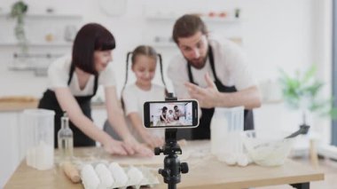 Beyaz bir aile, pişirme sürecini gösteren parlak ev mutfağında yemek pişirme dersleri videosu hazırlıyor..