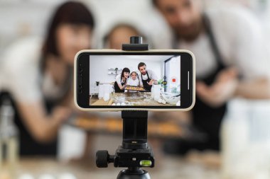 İki yetişkinin ve bir çocuğun ailesi mutfak kurabiyelerinde yemek içeriği yaratıyor. Birlikte eğlenirken onları kaydeden kameraya odaklan. Sahne neşeyi, etkinliği ve yaratıcılığı yakalar.