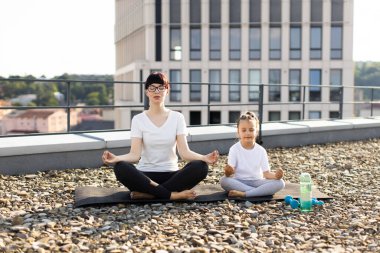 Kadın ve genç kız şehir çatısı üzerinde meditasyon yapıyorlar, farkındalık ve sükuneti ifade ediyorlar..